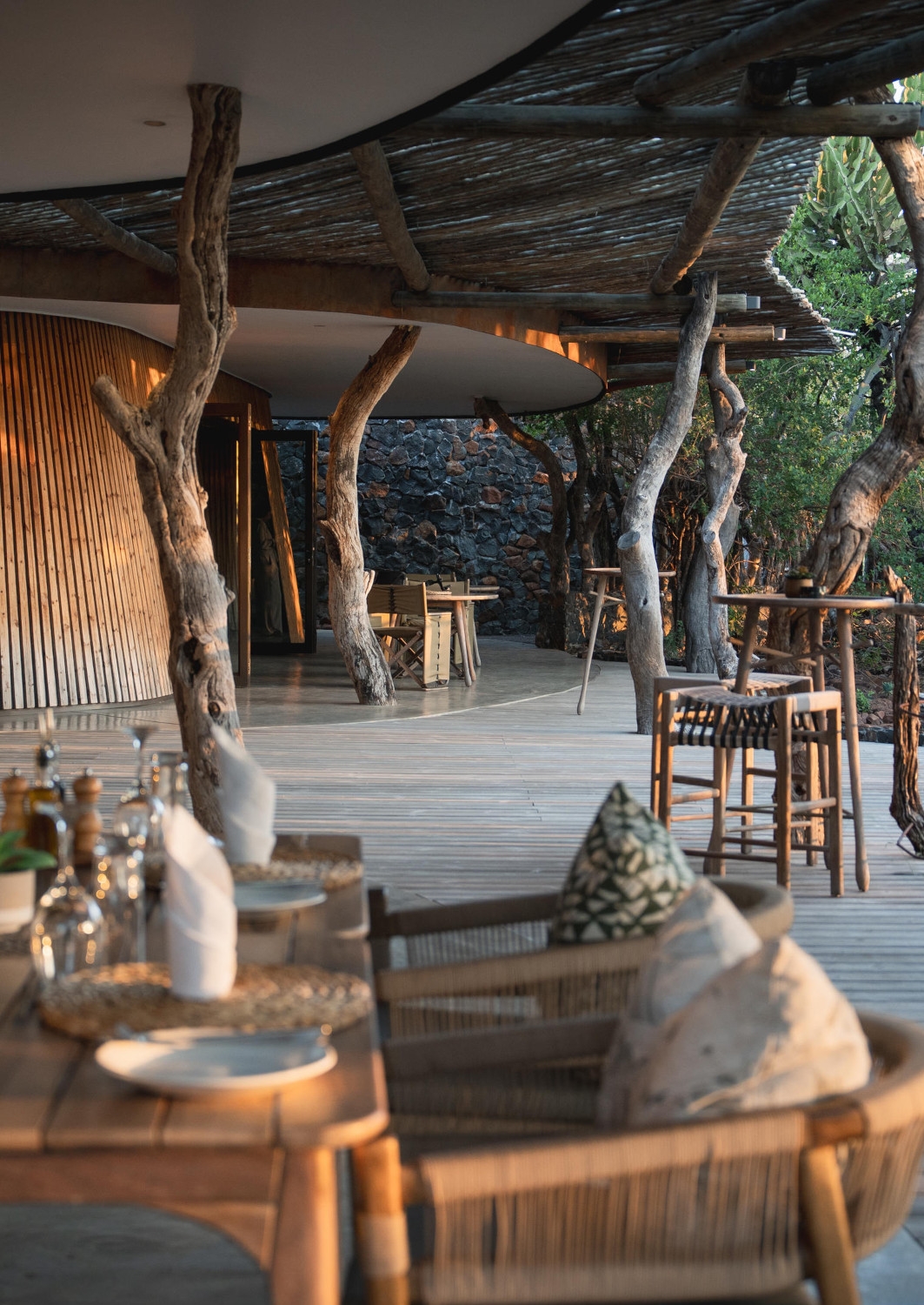 Covered wooden deck and dining area with several tables set for dinner and tree trunks growing up through the deck to the ceiling.