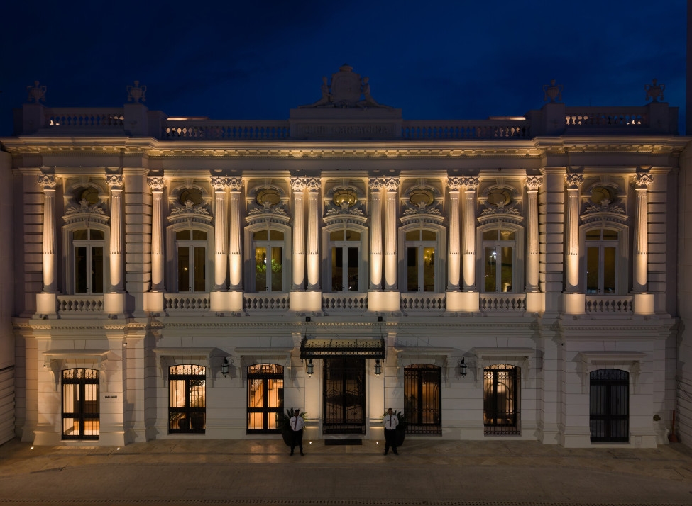 Exterior night view of the hotel with grand colonnades uplit by soft lighting.