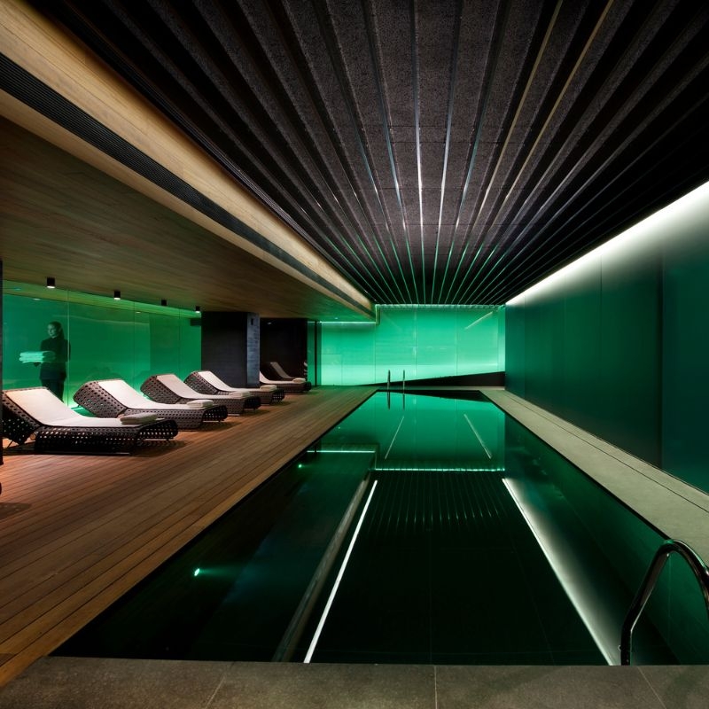 An indoor pool illuminated with green light, with several lounge chairs beside it