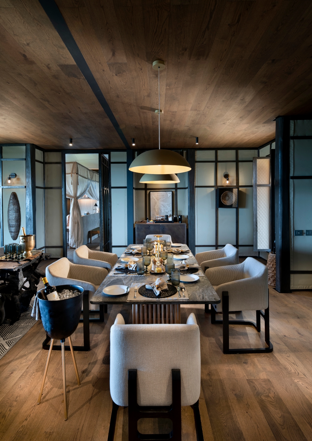 Interior shot of a dining table set for dinner with five grey chairs and two low-hanging lamps above.