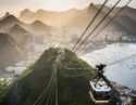 A cable car descends toward Sugar Loaf Mountain, with Rio de Janeiro city, a bay, and mountains in the background at sunset. luxury Brazil holidays.