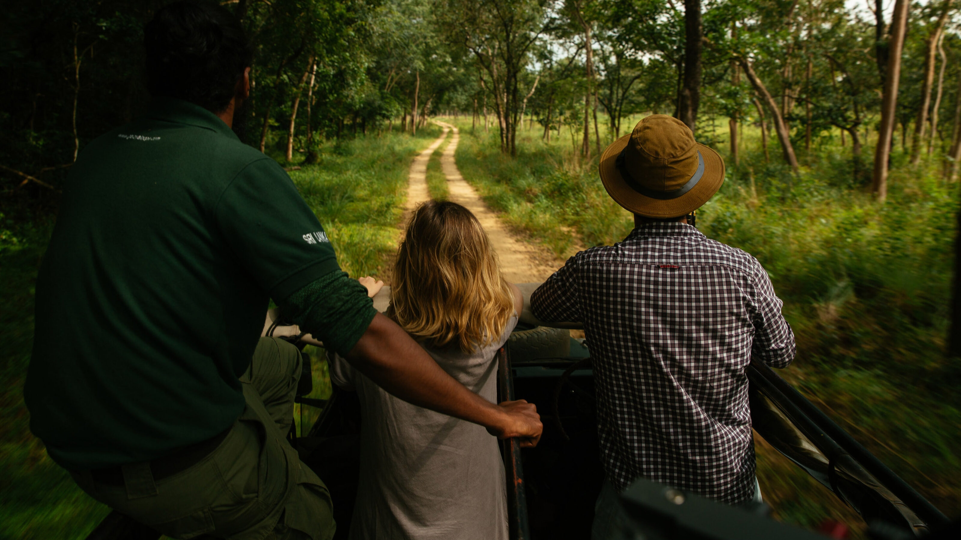 A family in an open safari vehicle looking out to a grassy trail.