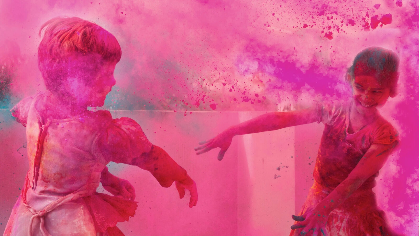 Two children playing amidst a thick cloud of vibrant pink celebration powder.