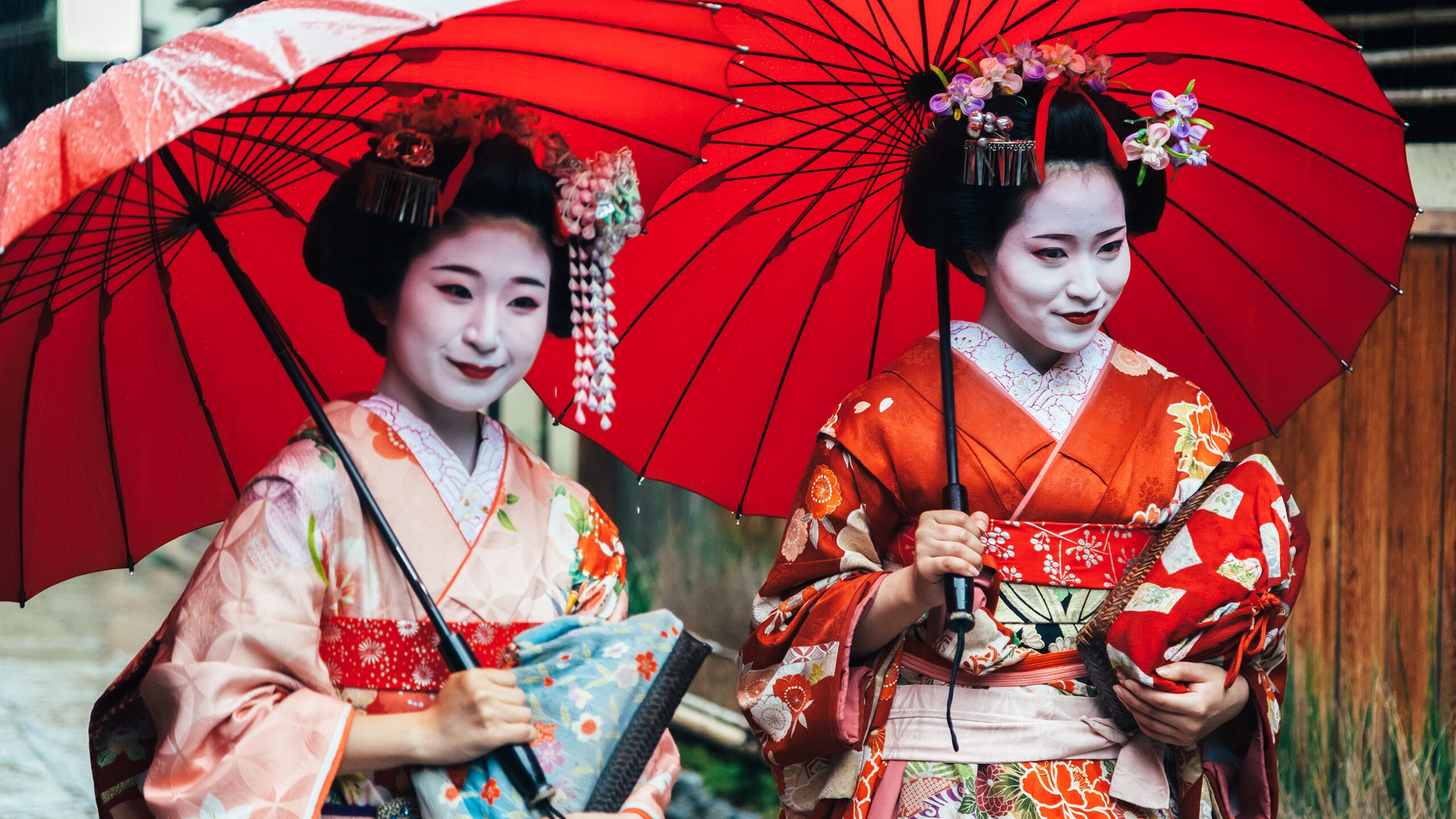 Private Japan Luxury Tours - Two maiko geisha walking on a street in Kyoto with red umbrellas