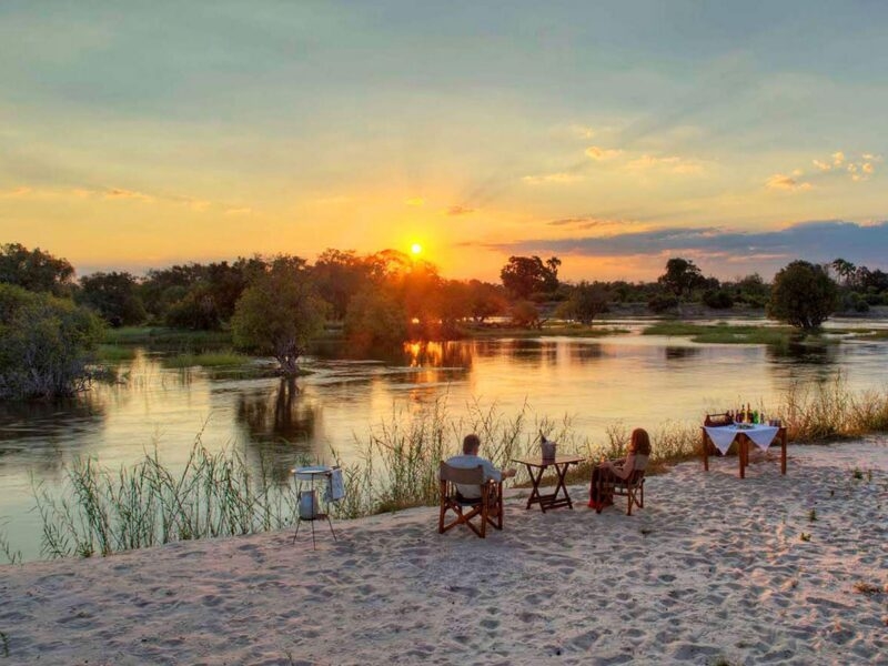 People enjoying a private sunset dinner on a riverbank during luxury Zambia tours.