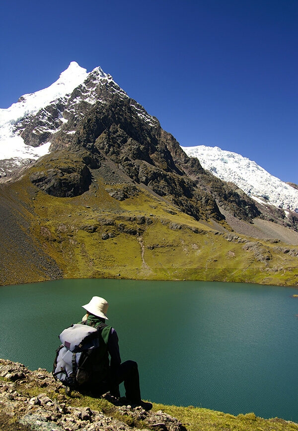 Jacada Peru - Person sitting by a still lake and snow capped mountain