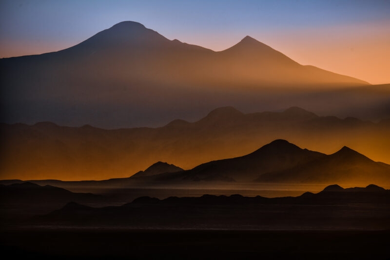Layers of mountains silhouetted against an orange and blue sky at sunset, with a darker foreground. Luxury Argentina trips.