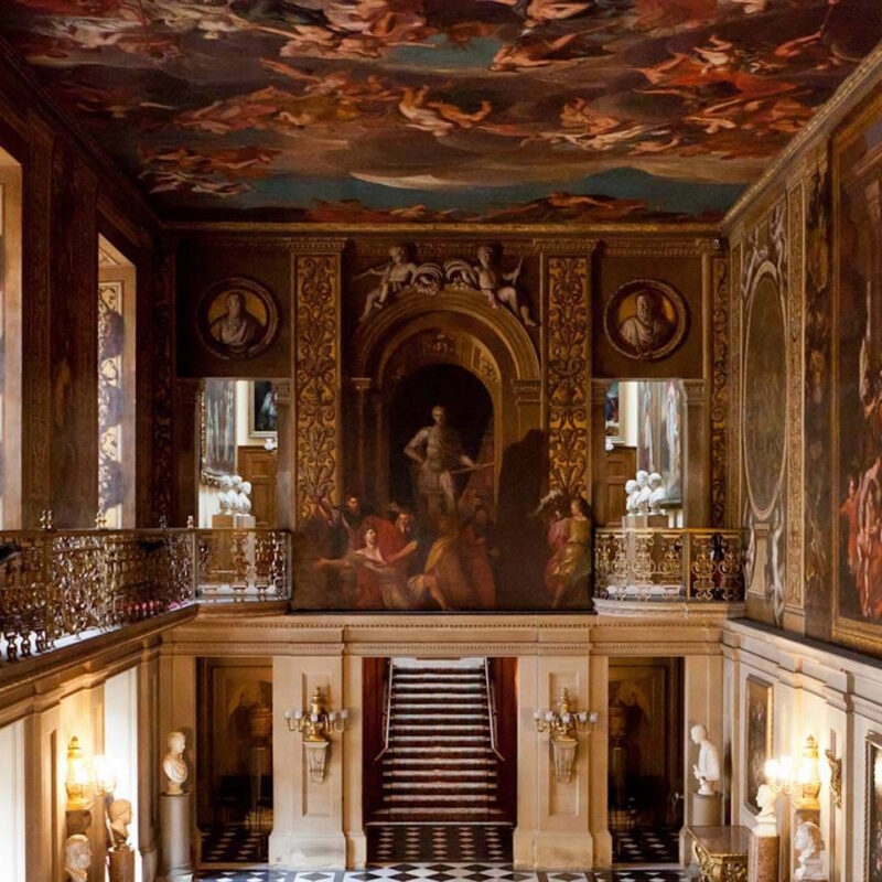 Grand interior hall featuring a red carpeted staircase, checkered floor, and a large painted ceiling mural.
