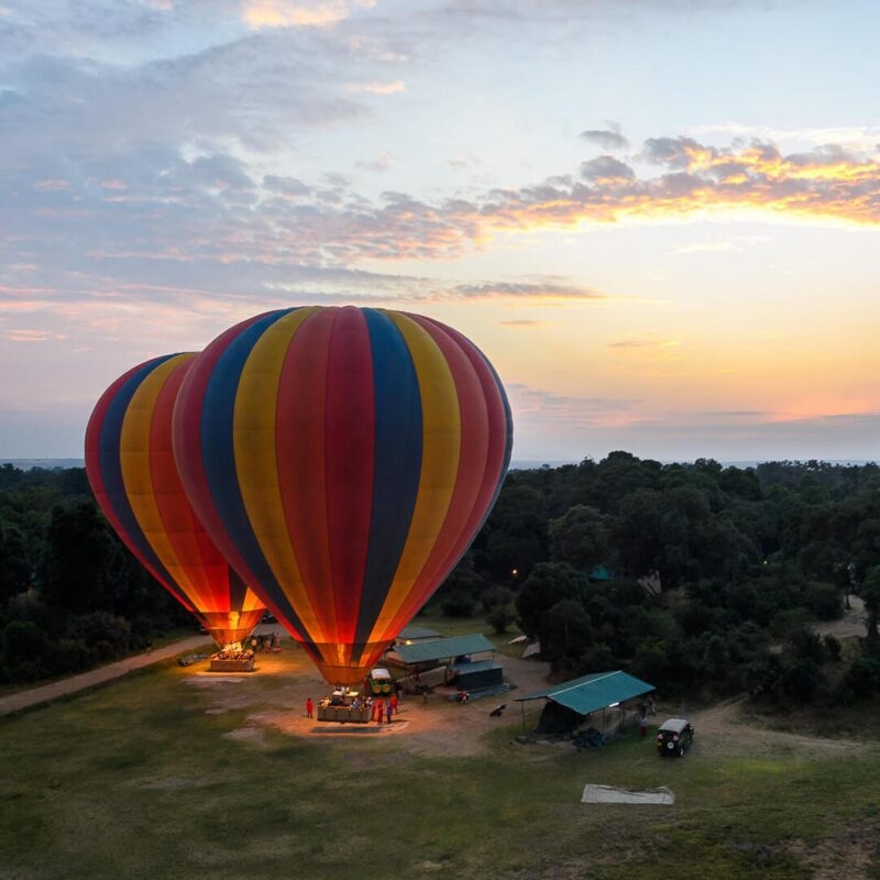 Two vibrant hot air balloons being inflated on a launch pad at sunrise during a luxury Kenya family safari.