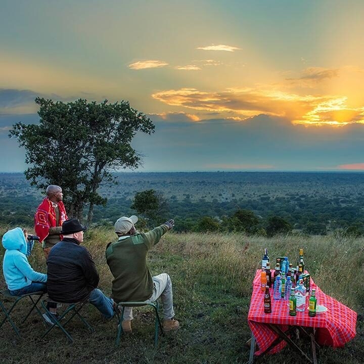 People sitting on a hillside with drinks on a red checkered table during a luxury Kenya family safari sunset.