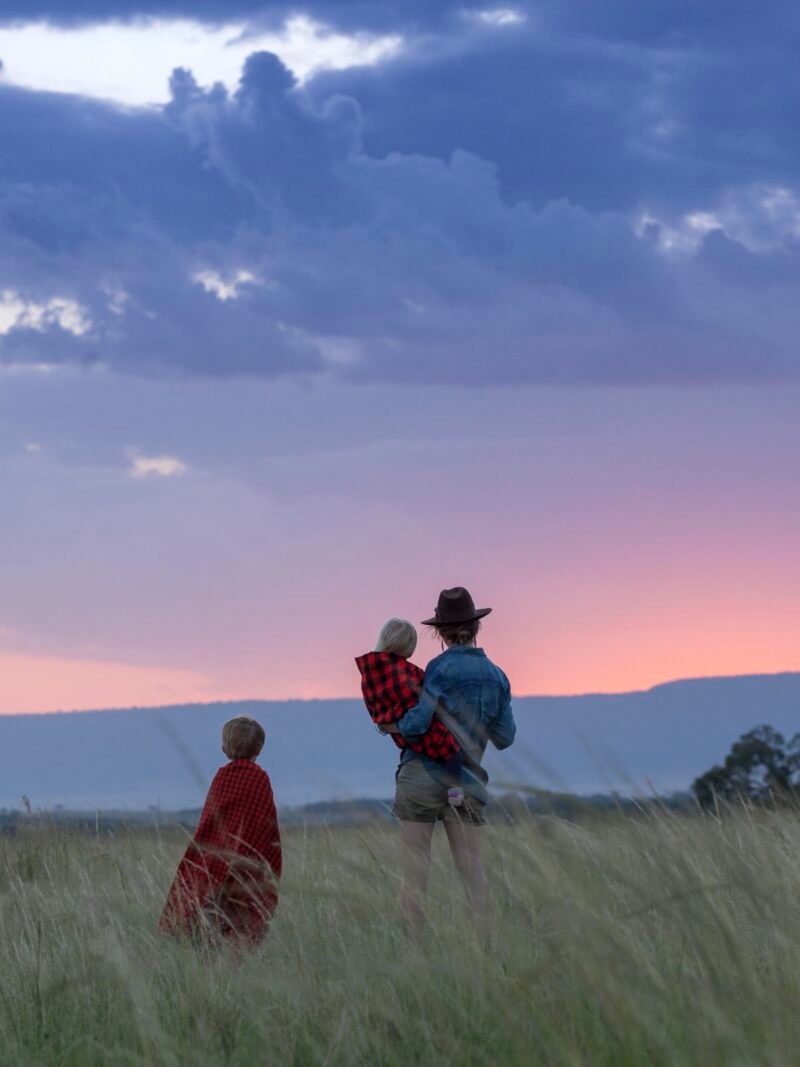 A woman and two children stand in a grassy field at dusk during a luxury Kenya family safari.