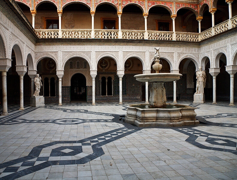 Ornate, arcaded Mudejar-style courtyard with tiled floor and central fountain. Perfect setting for luxury Spain holidays.