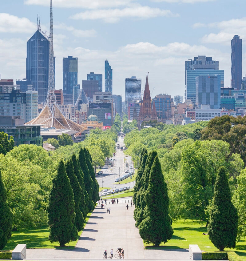 A wide, tree-lined path extends toward the Melbourne cityscape under a partly cloudy sky, an essential stop on luxury Australia tours.