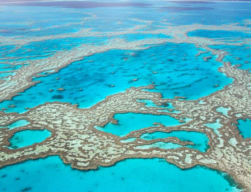 An aerial view of the Great Barrier Reef, showing shallow, complex coral formations in bright turquoise water, part of luxury Australia holidays.
