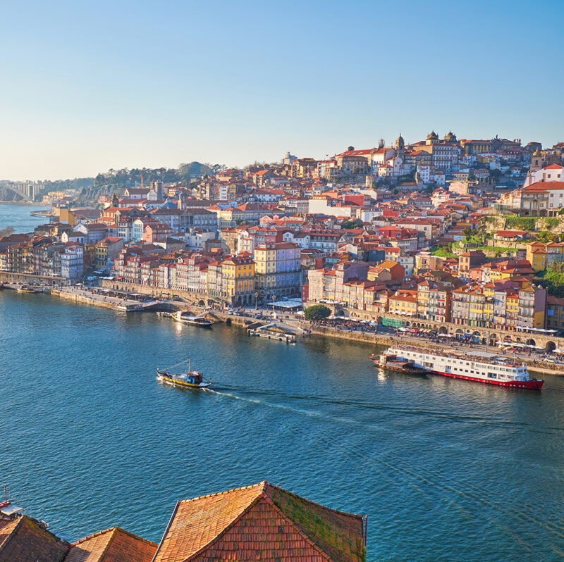 Panoramic view of Porto's colorful Ribeira district and the Douro River with boats, a top destination for luxury Portugal vacations.