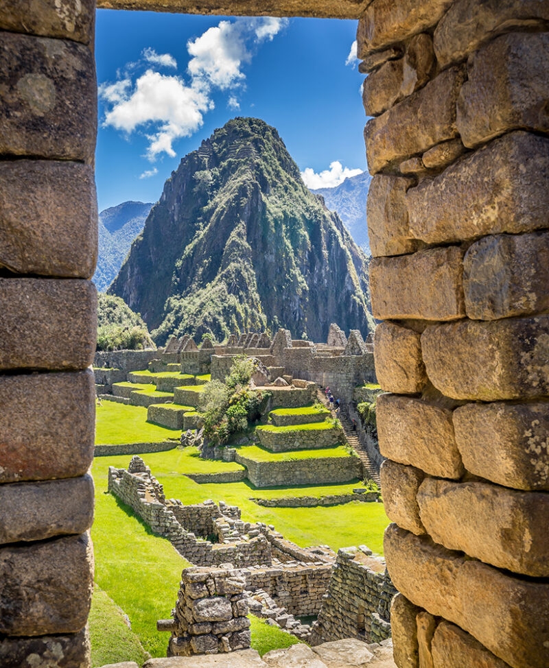 A view of Machu Picchu ruins, green grass, and Huayna Picchu mountain, framed by two weathered stone walls, suggesting luxury Machu Picchu vacations.