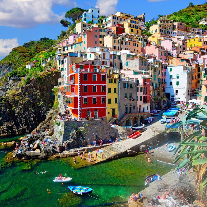 Colorful buildings on a cliff overlooking a clear green harbor during luxury Italy family holidays.
