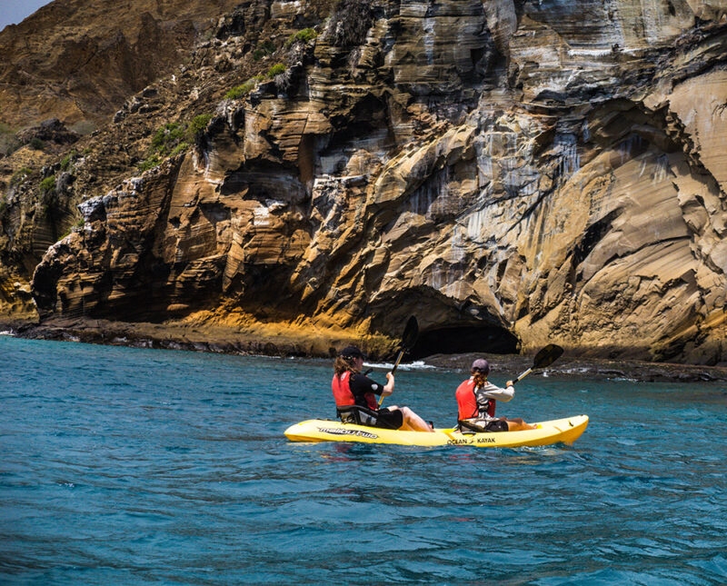 Two people kayaking past volcanic rock formations during luxury Ecuador holidays in the Galapagos.