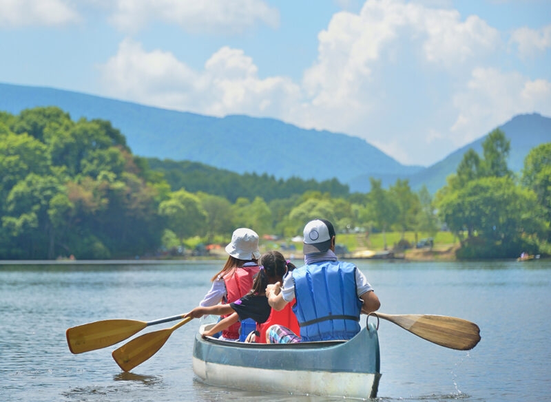 A family paddles a canoe across a calm blue lake surrounded by mountains and forests on luxury family tours to Japan.