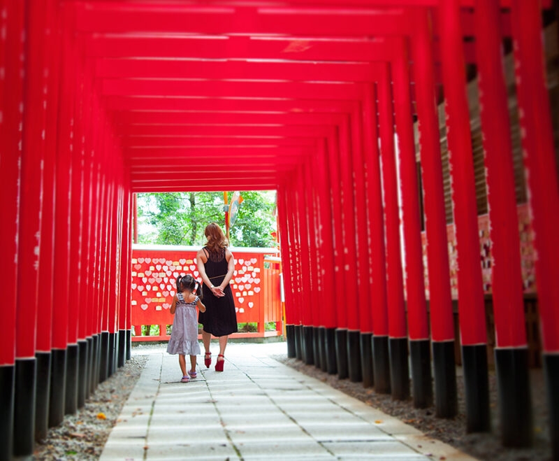 A woman and child walk through a tunnel of vibrant red torii gates while enjoying luxury family holidays to Japan.