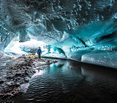 A person exploring a large ice cave with frozen ripples, part of Luxury Polar tours.