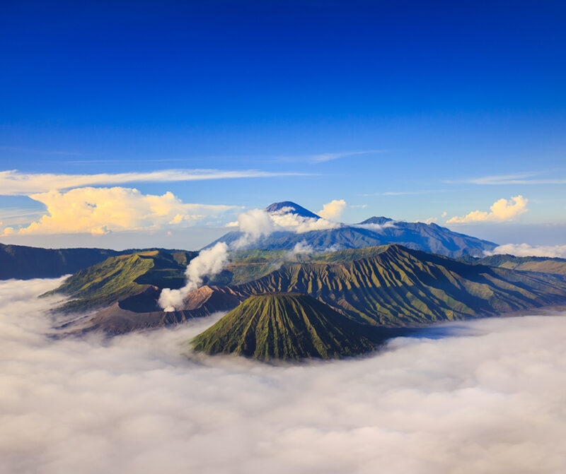 Aerial view of Mount Bromo volcanoes and surrounding mountains, with clouds settling in the valleys, offering luxury Indonesia holidays.