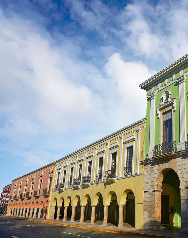 A street lined with a row of brightly colored colonial buildings with arches and balconies, found on luxury Mexico vacations.