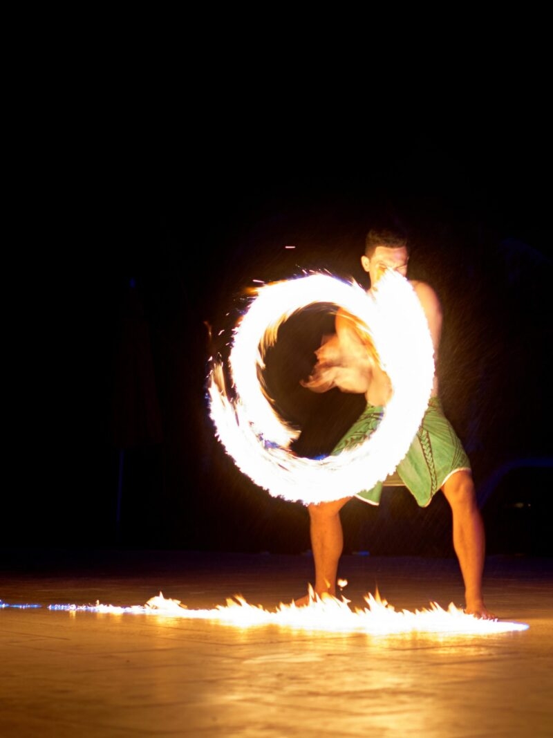 A man performing a fire dance with a flaming staff at night during luxury South Pacific holidays.