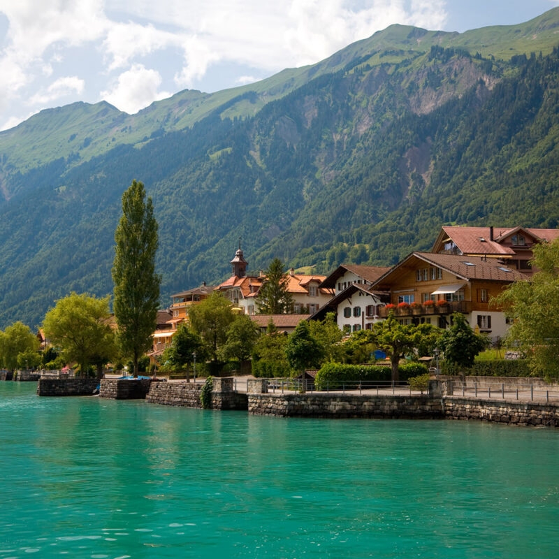 Lakeside village with traditional chalets nestled against steep green mountains during luxury Switzerland tours.