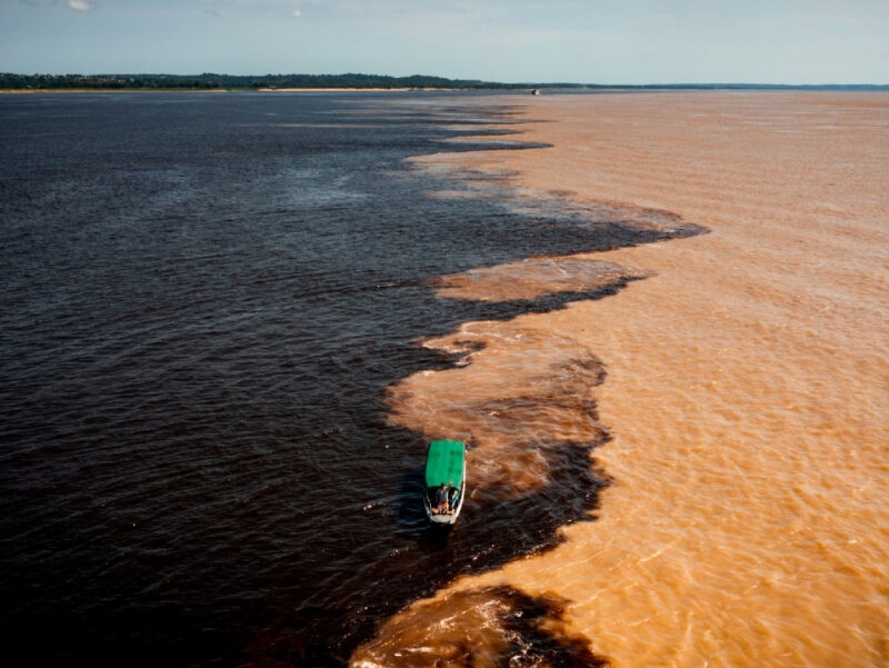 Aerial view of the "Meeting of Waters," where two rivers of distinct colors converge, with a boat in the center. luxury Brazil vacations.