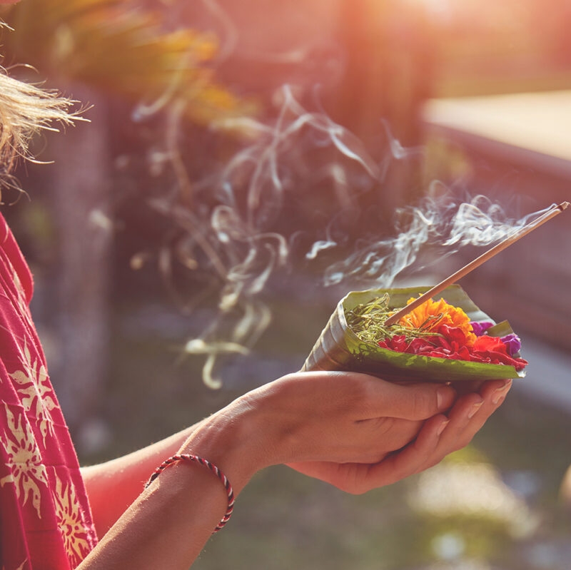 Hands holding a flower offering with burning incense on luxury Bali trips.