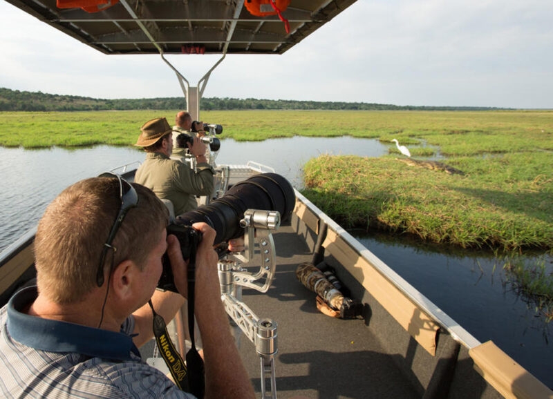 People on a long narrow boat taking photographs with long camera lenses in a wetland