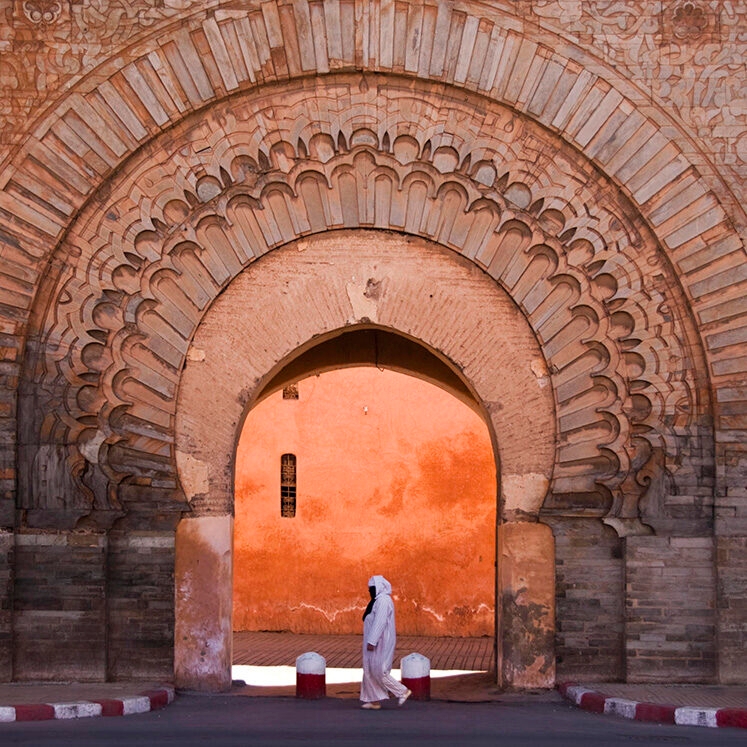 A person in white traditional clothing walks through a massive stone arch on luxury Africa honeymoon vacations.