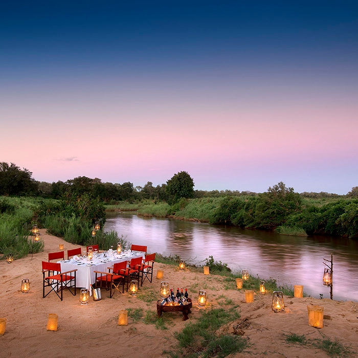 A romantic dinner table with red chairs by a river during luxury Africa honeymoon trips.