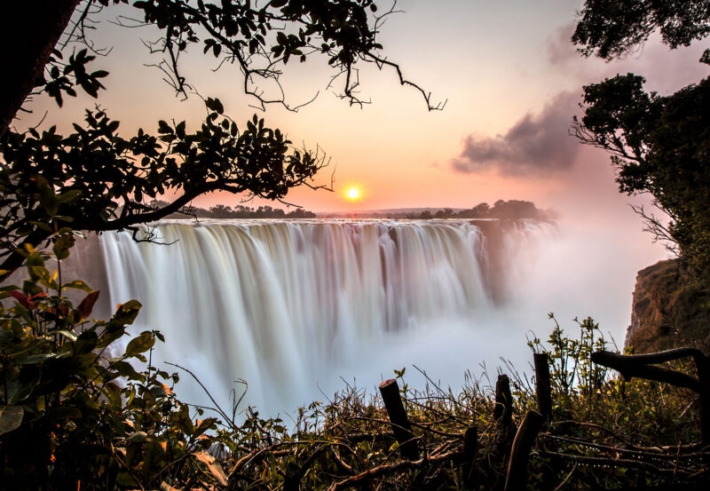 A wide waterfall at sunset with mist and trees, a highlight of luxury Africa honeymoon holidays.