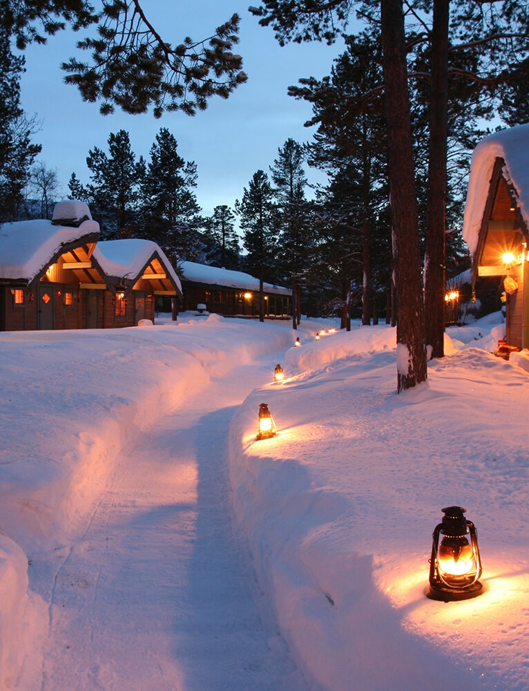 Snowy huts lit by soft glowing lanterns in the Norwegian wilderness