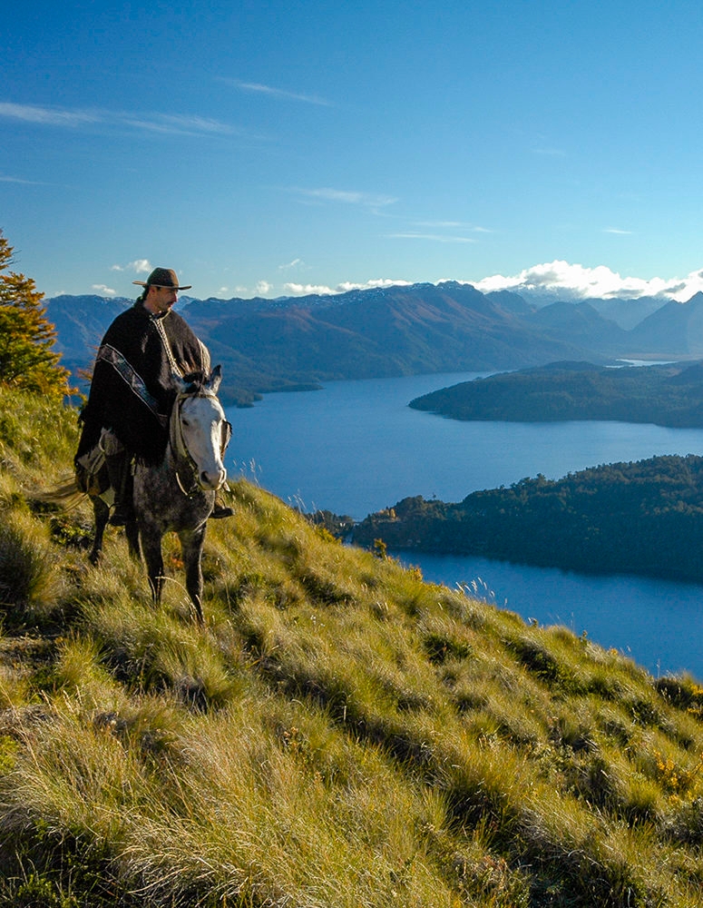 A person riding a horse on a high grassy path above a blue lake