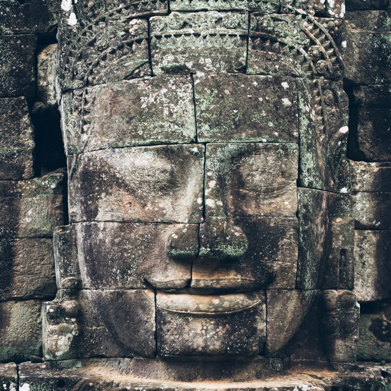 Ancient serene stone face carving at a temple site during luxury grand tours.