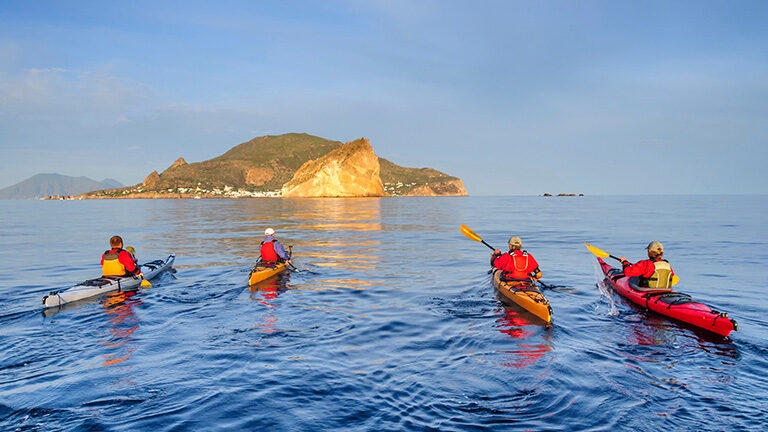 A group of people kayaking in the sea with a small green island behind