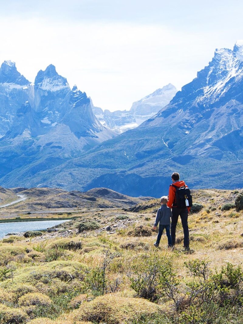 A group of people walking through a valley with tall snowy mountains ahead of them