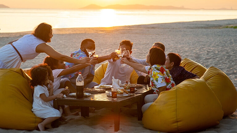Group of multiethnic family friends enjoy dinner party together on the beach at sunset.
