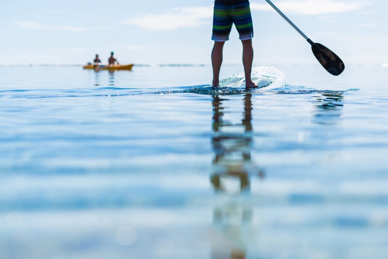 adventure trips - Close up of a person's legs as they stand on a paddle board in calm water