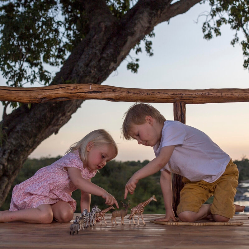 Two children playing with plastic safari animals on a wooden deck