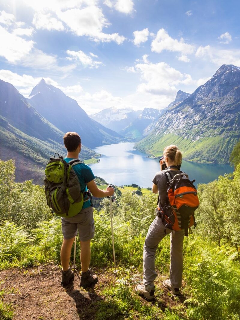 Two hikers at viewpoint in mountains with lake, sunny summer