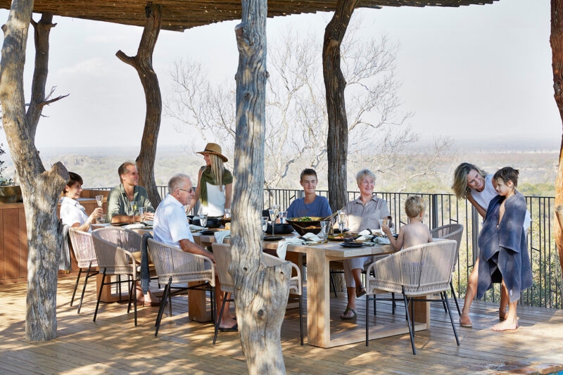 Family members sitting at a long wooden table on an outdoor deck during luxury Family vacations.