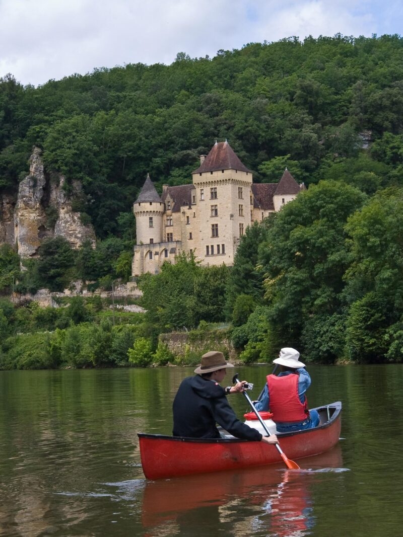 Young people canoing on the Dordogne River in France, past medieval castles and striking ancient cliffs. The lad in the back of the canoe holds a small camera.