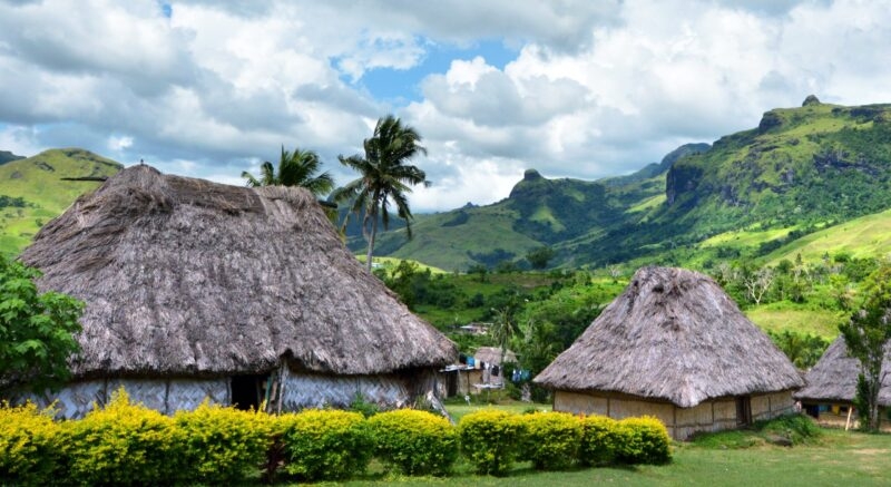 Traditional thatched-roof huts in a green valley with mountain peaks in the background during luxury Fiji trips.