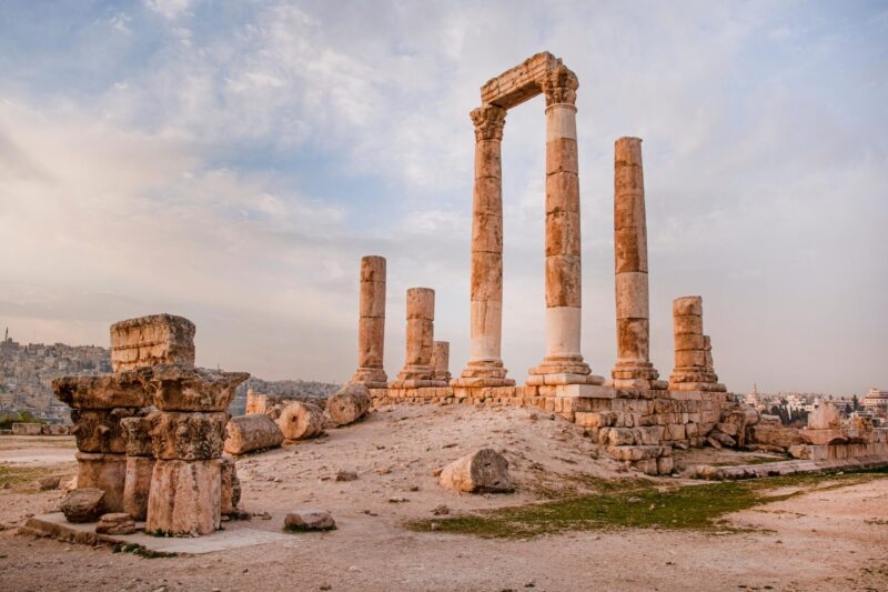 The ruins of the Roman Temple of Hercules, featuring tall columns and stone blocks, stand on a hilltop overlooking a city. A luxury Middle East tour.