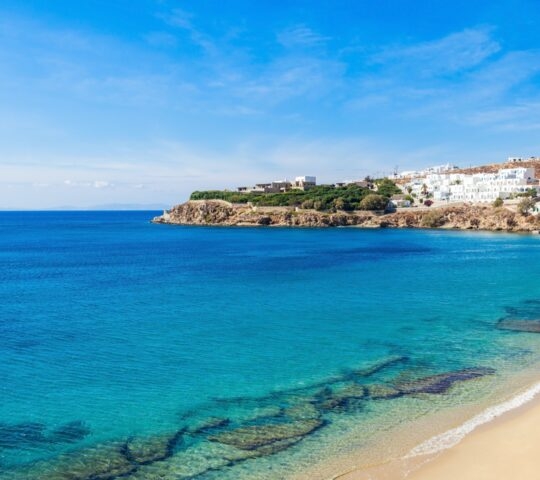 On the beach in Mykonos, Greece, crystal blue waters lap the golden sands