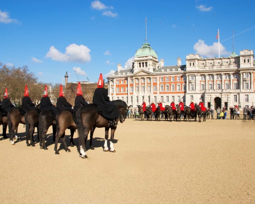 Mounted soldiers on black horses at Horse Guards Parade in London under a clear blue sky.